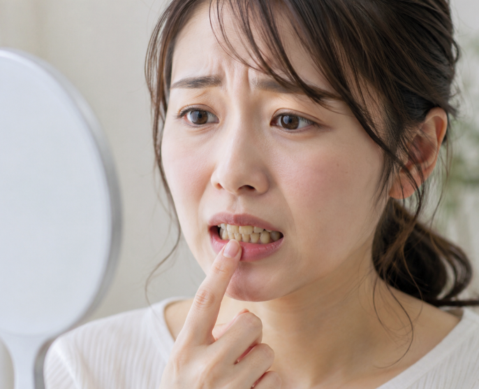 鏡を見ながら歯の状態を気にしている女性のイメージ